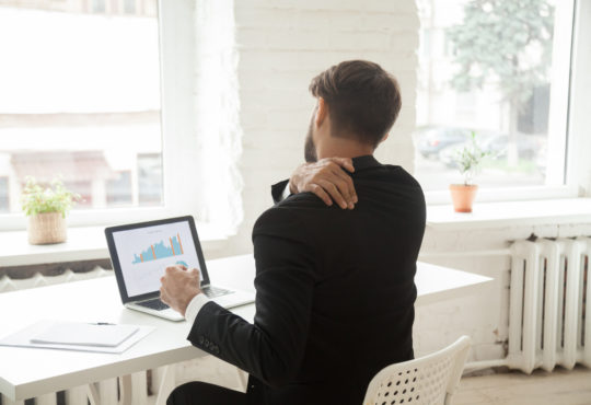 Tired businessman stretching at workplace exhausted after work