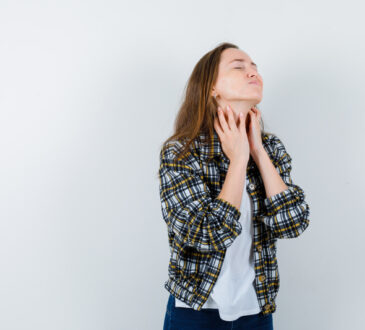 Young lady in t shirt, jacket touching skin on her neck and looking tired , front view.