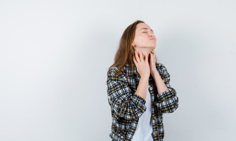 Young lady in t shirt, jacket touching skin on her neck and looking tired , front view.