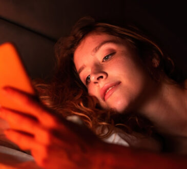 Young girl with smartphone in a bed. red illumination