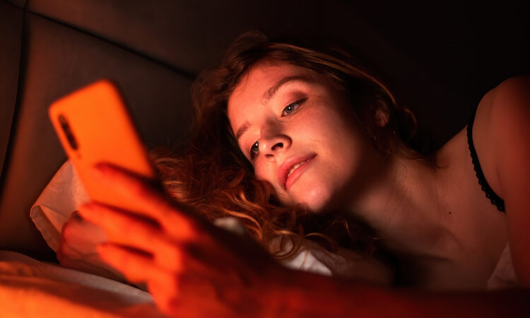 Young girl with smartphone in a bed. red illumination